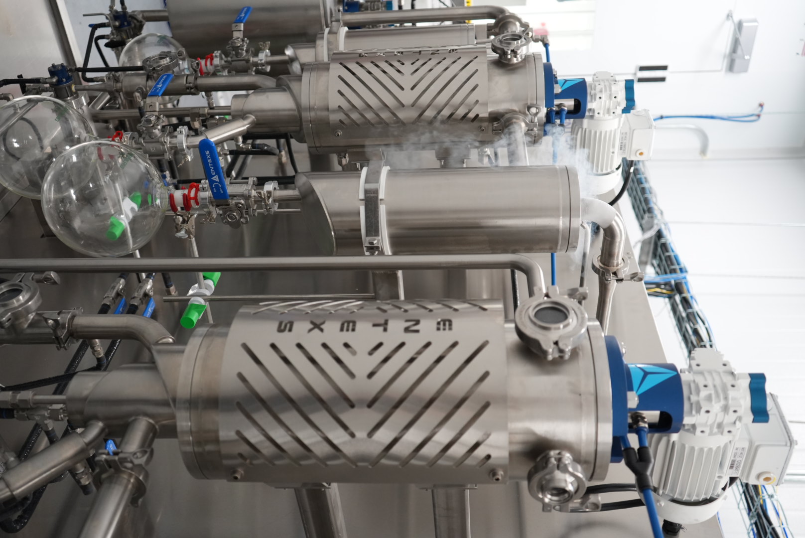 Stainless-steel extraction equipment with blue motors and glass collection vessels inside the LP lab